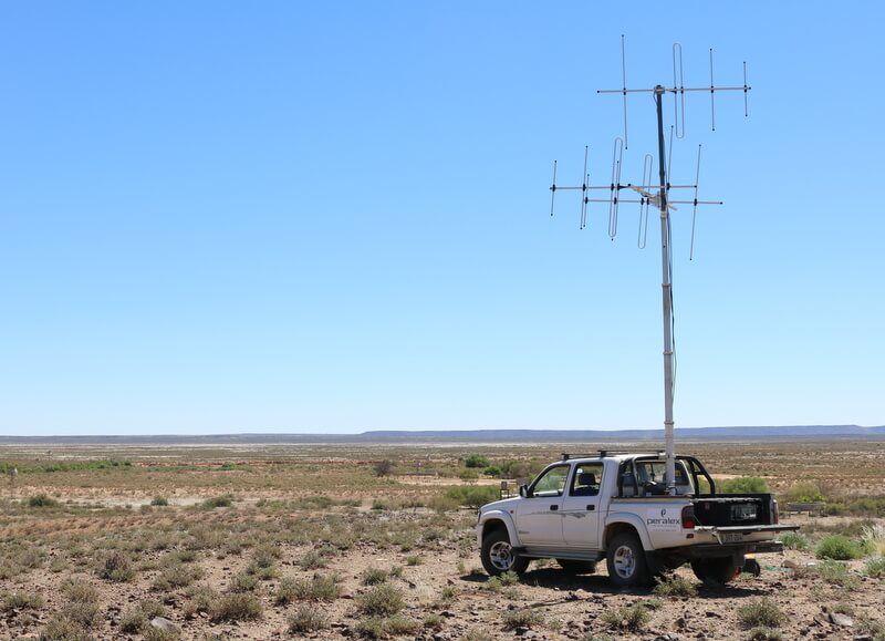 A passive radar receiving antenna on a mast beside a vehicle in open country